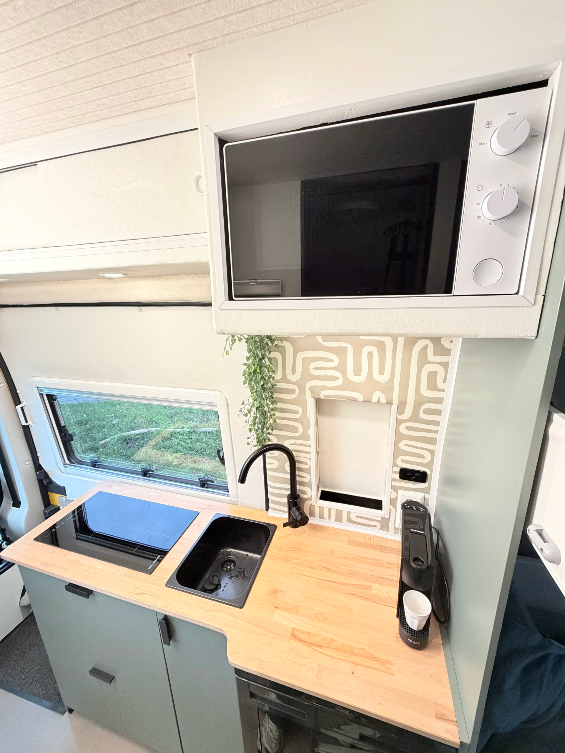 “Compacte offgrid keuken in de Happy Vanlife camper met kookplaat, spoelbak, houten werkblad en ingebouwde magnetron.”