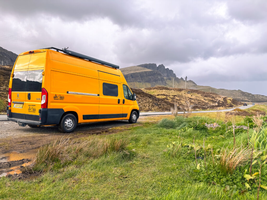 Gele buscamper rijdt door de Schotse Hooglanden tijdens een offgrid roadtrip.